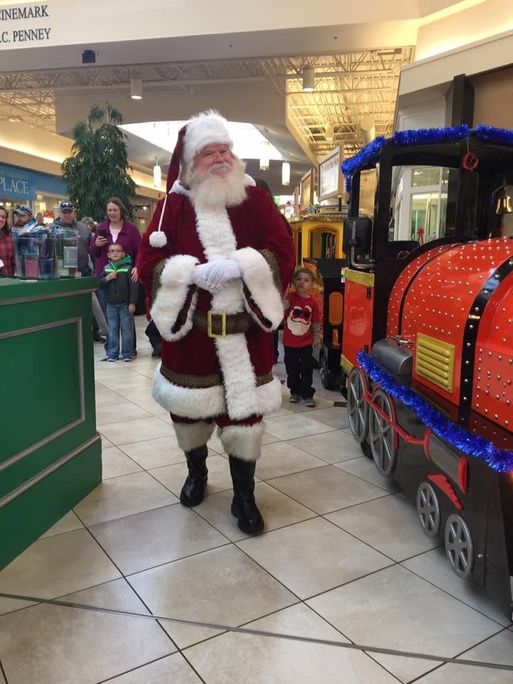 Santa Claus standing beside the All Smiles Aboard trackless train