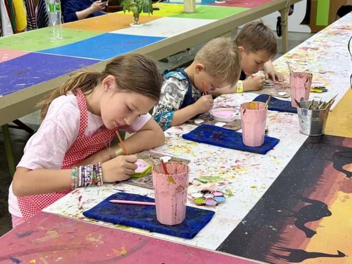 Emma painting pottery at a craft table next to her little brothers