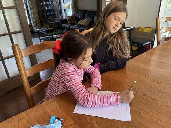 Emma helping a little girl with her writing at the table
